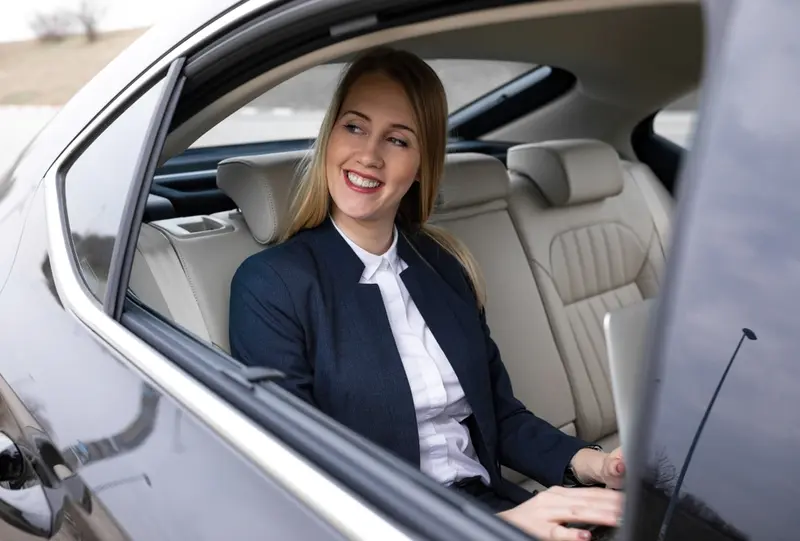 A woman sitting in the back seat of a luxury black car during a trip, staring out through the open window, symbolizes stress-free long long-distance transportation to and from Galveston